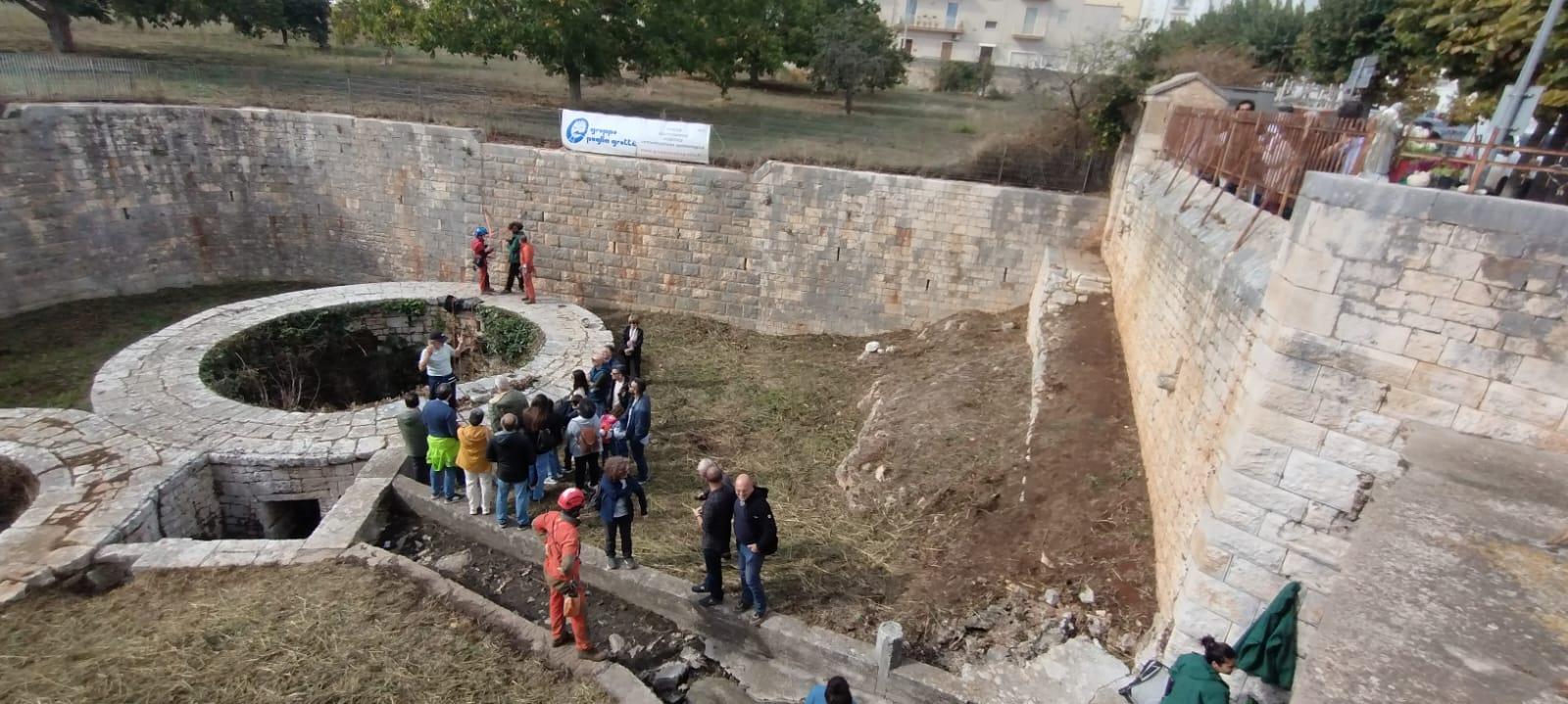 Veduta dall’alto del sito delle Gravinelle: i visitatori ascoltano le spiegazioni dei soci del Gruppo Puglia Grotte accanto ai pozzi