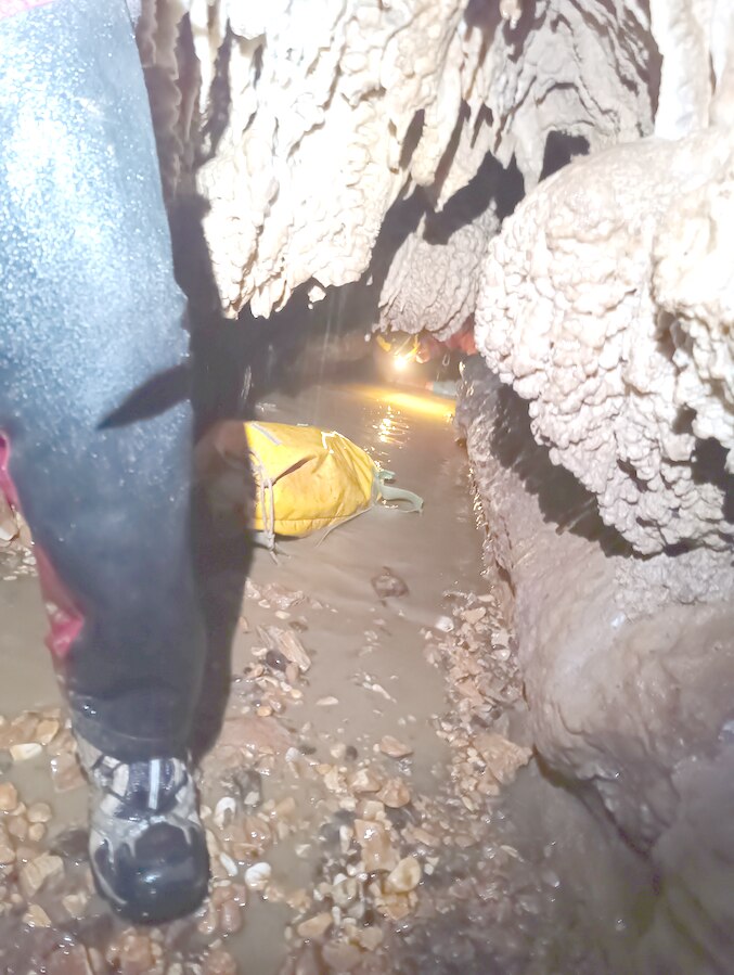 Meandro allagato con acqua e fango, sacco da speleologia in primo piano