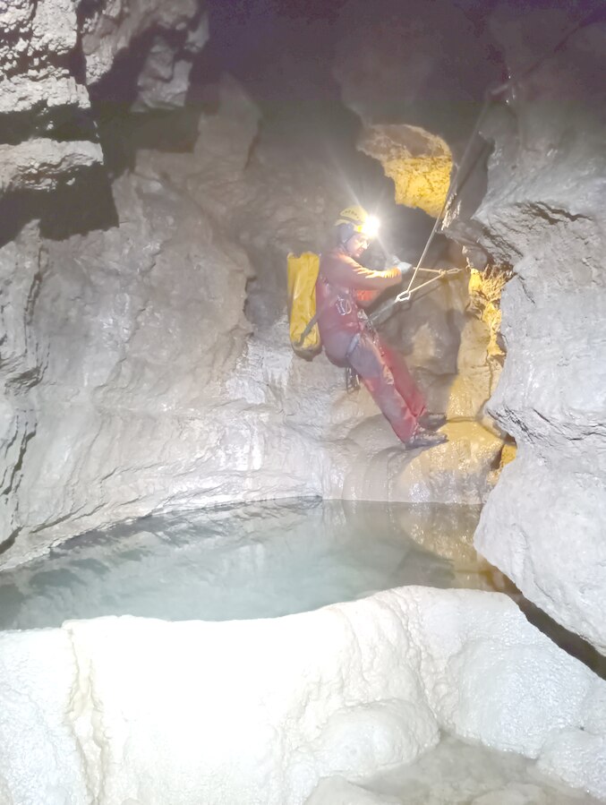 Speleologo su un traverso attrezzato accanto a una pozza d'acqua